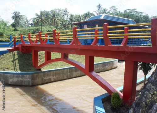 a bridge with red yellow and blue colors in temanggung district, central java at noon. water flows in a river under the bridge © MA