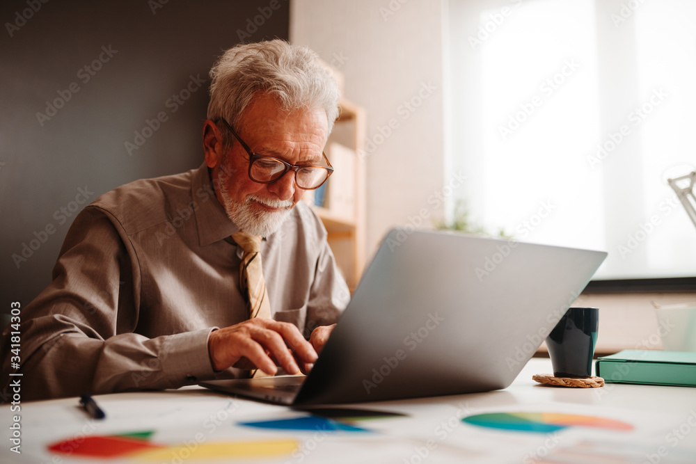 Portrait of elderly man working with laptop while sitting in his bright office during working hours. Portrait of elderly man working with laptop while sitting in his bright office during working hours.