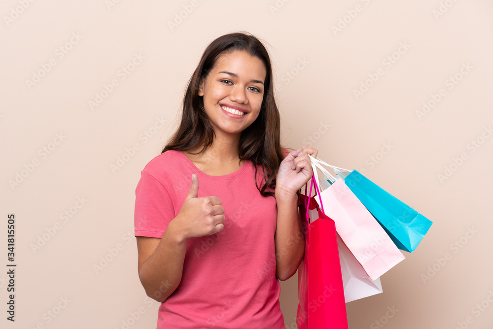 Young Colombian girl with shopping bag over isolated background holding shopping bags and with thumb up Young Colombian girl with shopping bag over isolated background holding shopping bags and with thumb up