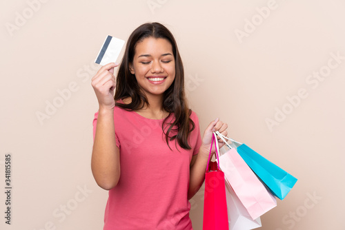 Young Colombian girl with shopping bag over isolated background holding shopping bags and a credit card