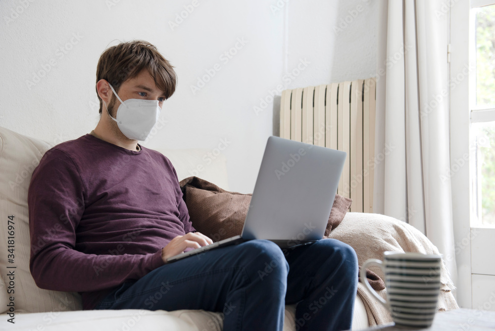 man working on his computer from the couch with a face mask man working on his computer from the couch with a face mask
