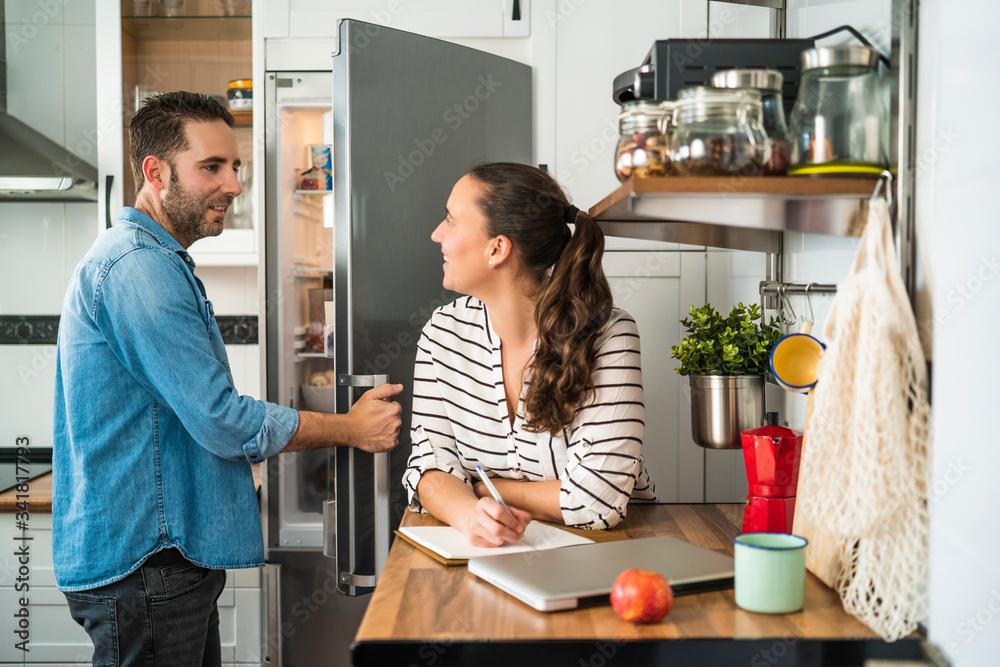 Young Man and Woman Couple talking and making the shopping list in their kitchen at home. Working at home and staying at home. Young Man and Woman Couple talking and making the shopping list in their kitchen at home. Working at home and staying at home.
