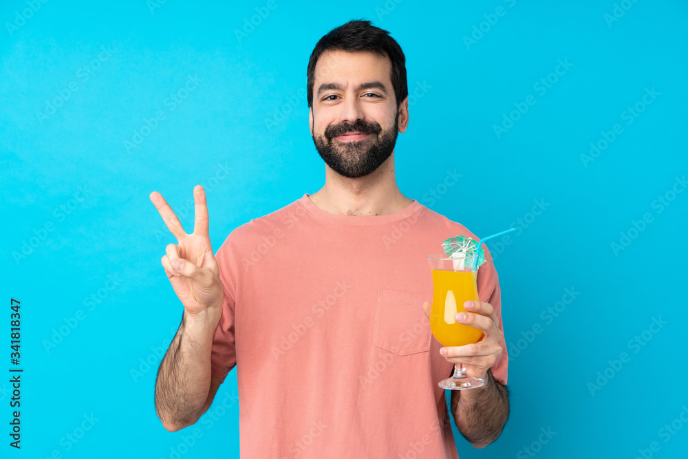 Young man over holding a cocktail over isolated blue background showing victory sign with both hands Young man over holding a cocktail over isolated blue background showing victory sign with both hands