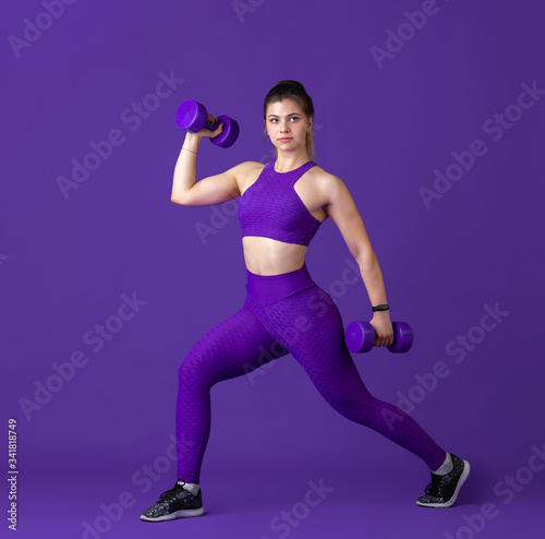 Strong. Beautiful young female athlete practicing in studio, monochrome purple portrait. Sportive fit caucasian model with weights. Body building, healthy lifestyle, beauty and action concept.