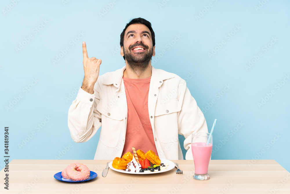 Man at a table having breakfast waffles and a milkshake pointing up and surprised Man at a table having breakfast waffles and a milkshake pointing up and surprised