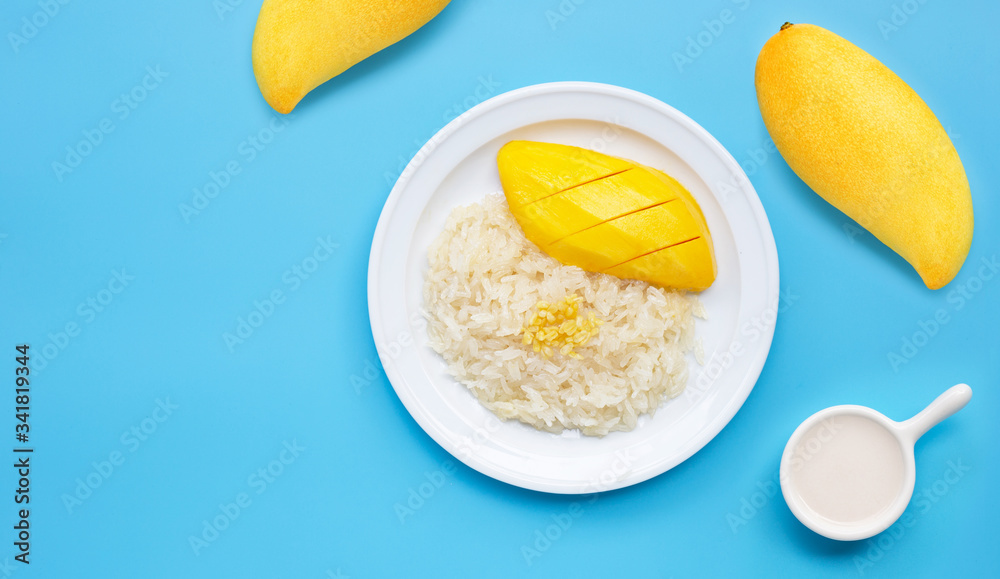 Thai dessert, sweet sticky rice with mango and coconut milk on blue background.