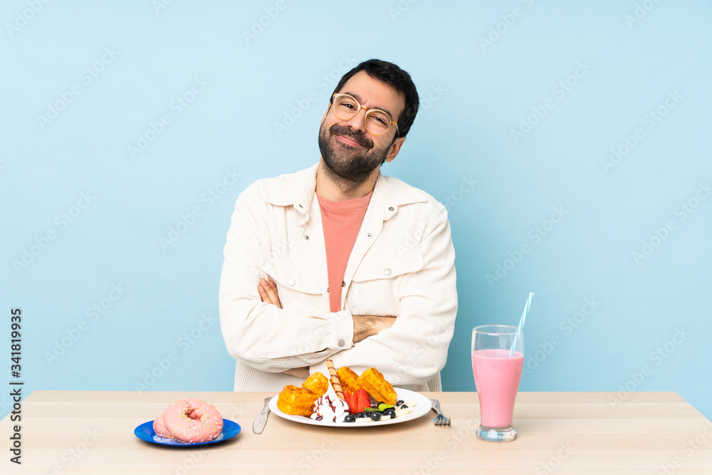 Man at a table having breakfast waffles and a milkshake with glasses and smiling Man at a table having breakfast waffles and a milkshake with glasses and smiling