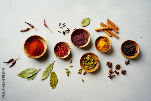 Fototapeta Naklejka Na Ścianę i Meble -  Various colorful spices in wooden bowls on concrete background. Top view. Different types of pepper, turmeric, paprika, rosemary, chili, cardamom, cinnamon, anise, cloves.
