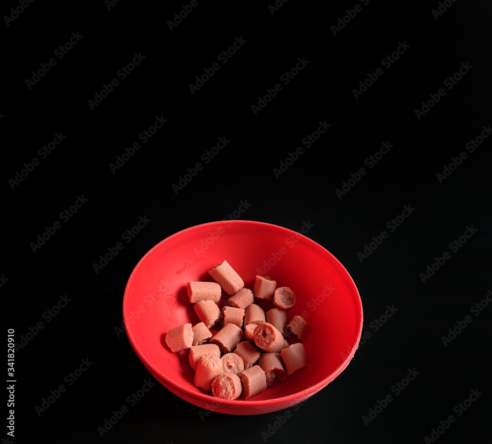Red plate with pieces of sausage on black background. Healthy snack concept Red plate with pieces of sausage on black background. Healthy snack concept