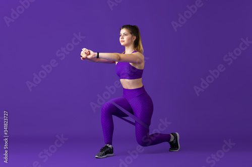 Strong. Beautiful young female athlete practicing in studio, monochrome purple portrait. Sportive caucasian fit model with elastics. Body building, healthy lifestyle, beauty and action concept.