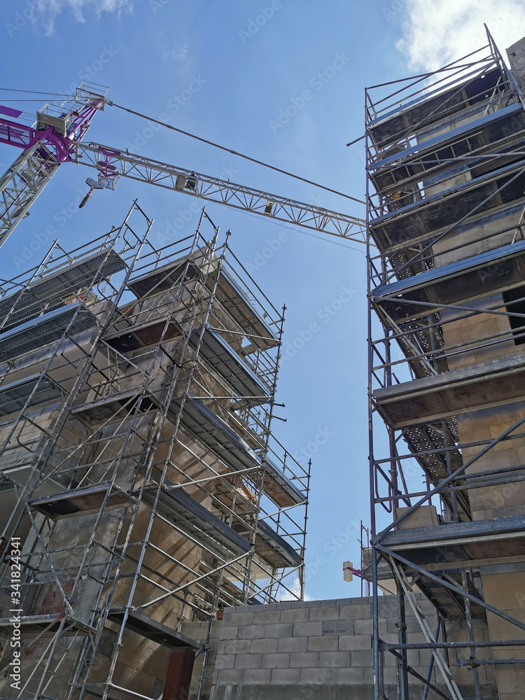 
building crane and building under construction in scaffolding against the blue sky
