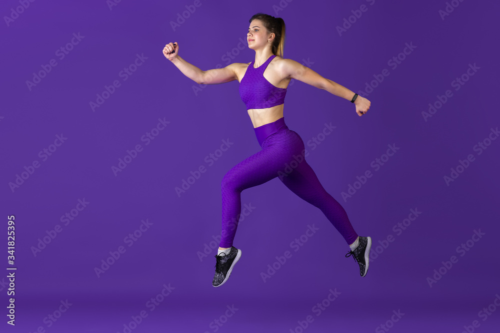 In jump. Beautiful young female athlete practicing in studio, monochrome purple portrait. Sportive caucasian fit model training. Body building, healthy lifestyle, beauty and action concept.