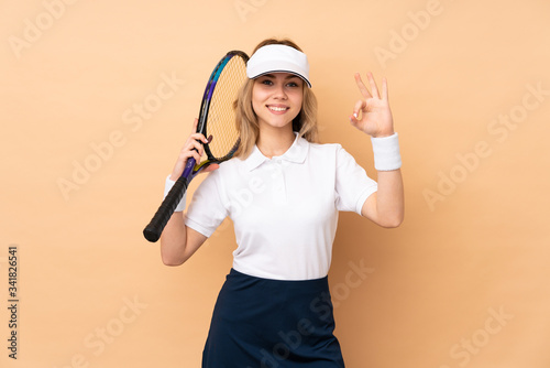Teenager Russian girl isolated on beige background playing tennis and making OK sign