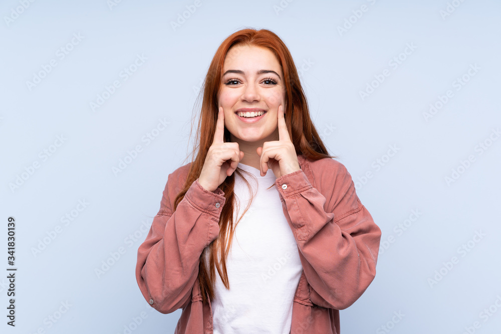 Redhead teenager girl over isolated blue background smiling with a happy and pleasant expression