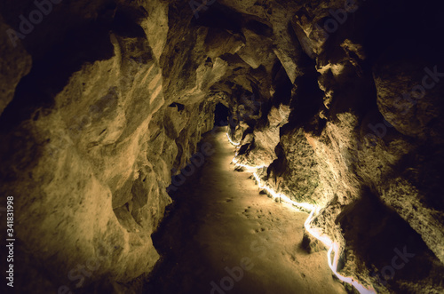 straight underground path in a stone cave illuminated by yellow light with rock wall and a black hole at the end photo