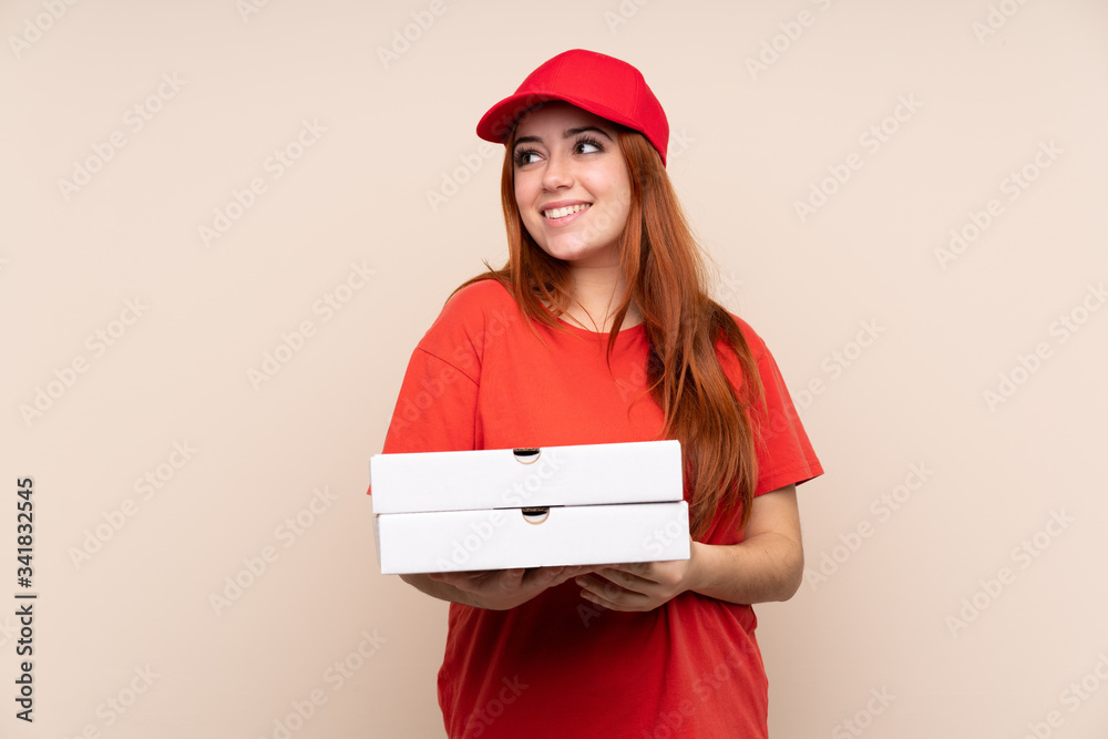 Pizza delivery teenager girl holding a pizza over isolated background laughing and looking up Pizza delivery teenager girl holding a pizza over isolated background laughing and looking up