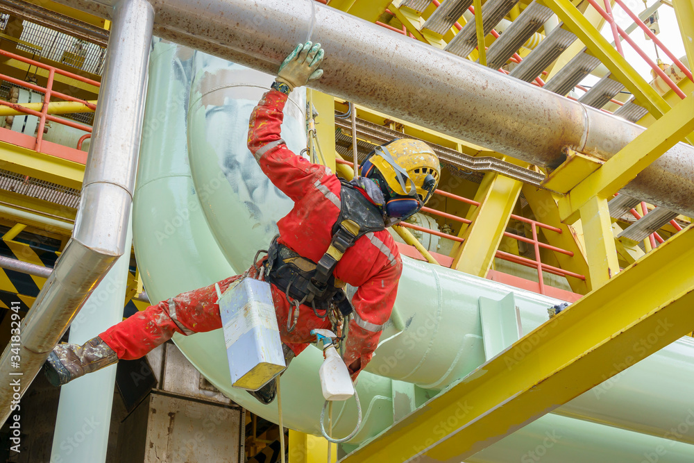 Working at height. A rear view of abseilers wearing red coverall and Personal Protective
