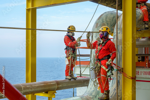 Working at height. A group of abseilers wearing red coverall and Personal Protective Equipment (PPE) standing on the piepeline managing their rope access with background open sea.