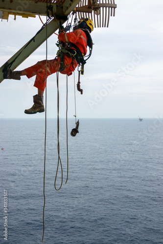 Working at height. A group of abseilers wearing red coverall and Personal Protective Equipment (PPE) hanging under access way platform to check the corrosion of the structure.