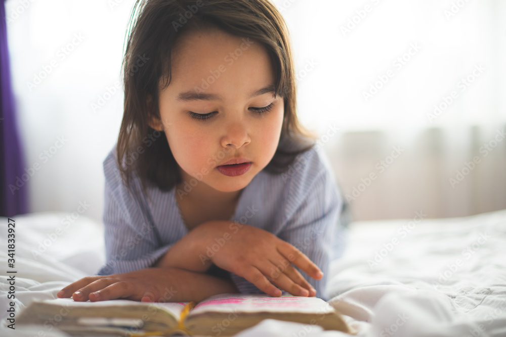Little girl reading from bible while she is in bed in the morning Little girl reading from bible while she is in bed in the morning