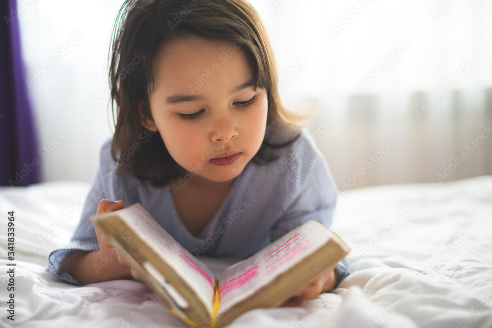 Little girl reading from bible while she is in bed in the morning Little girl reading from bible while she is in bed in the morning