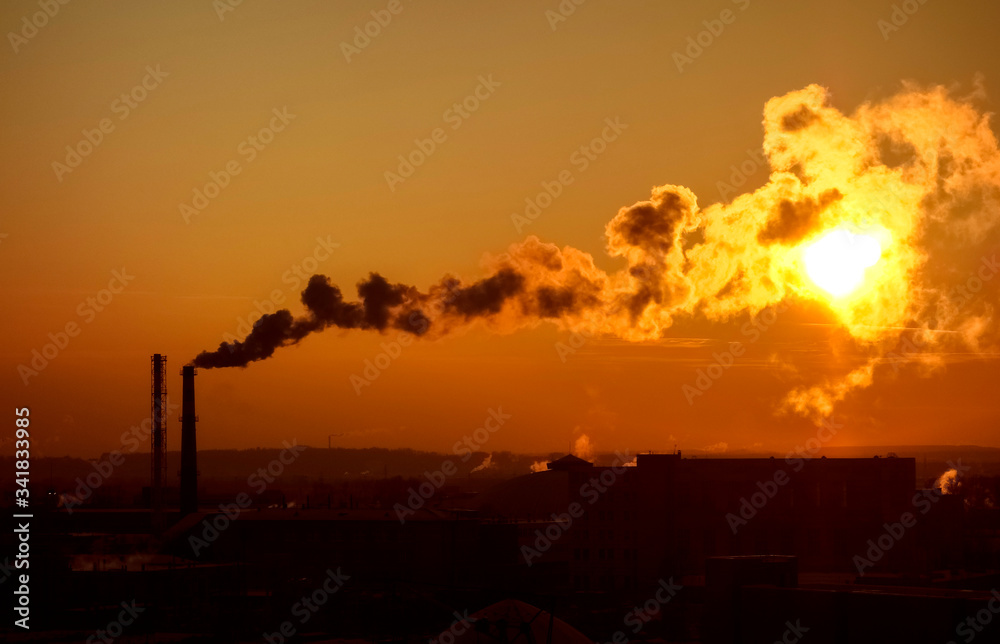 Naklejka premium Smoke comes out of the pipes into the sky, against the background of the setting sun