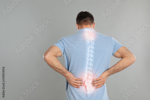 Man suffering from pain in spine on grey background photo