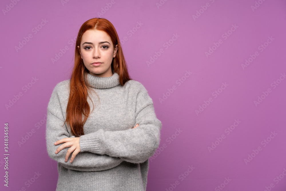 Redhead teenager girl over isolated purple background keeping arms crossed