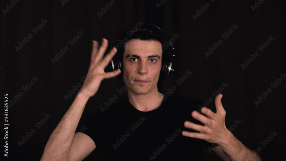 Caucasian man in black and in headphones, funny dancing in front of the camera and listening to music, on black background, portrait. Caucasian man in black and in headphones, funny dancing in front of the camera and listening to music, on black background, portrait.