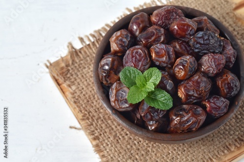 dried date and green mint in a bowl on white wooden table.