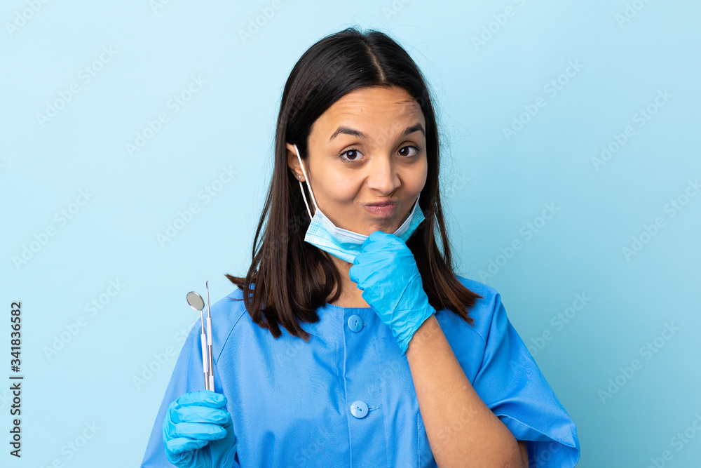 Young brunette mixed race dentist woman holding tools over isolated background thinking Young brunette mixed race dentist woman holding tools over isolated background thinking