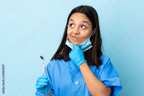 Young brunette mixed race dentist woman holding tools over isolated background thinking an idea while looking up