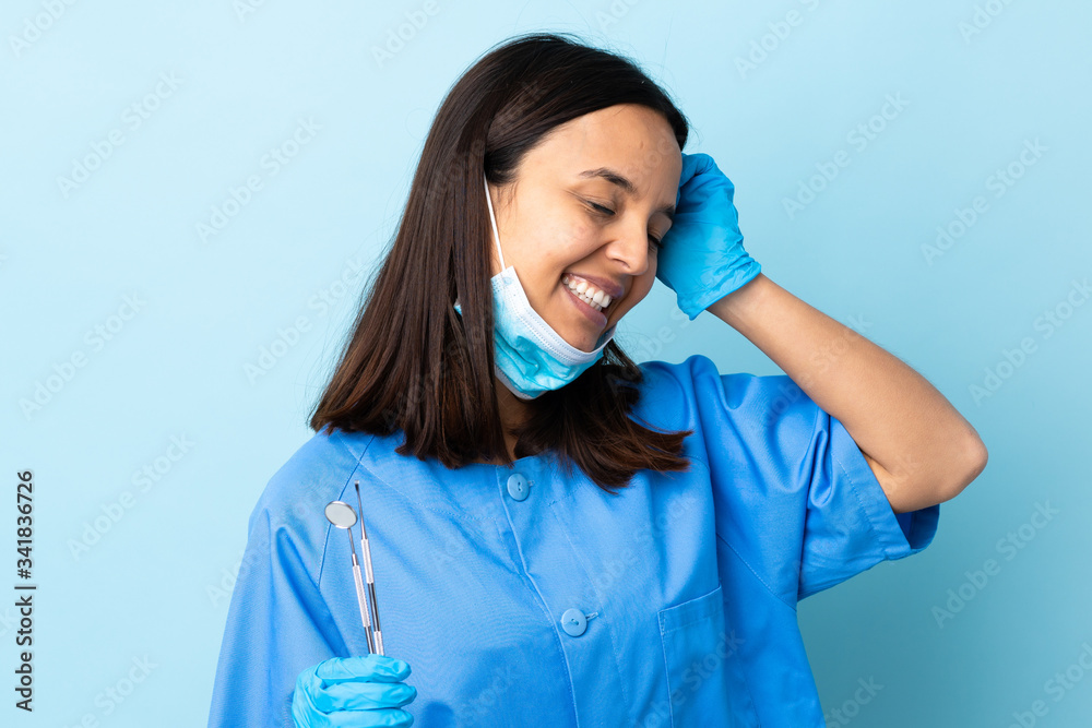 Young brunette mixed race dentist woman holding tools over isolated background smiling a lot Young brunette mixed race dentist woman holding tools over isolated background smiling a lot