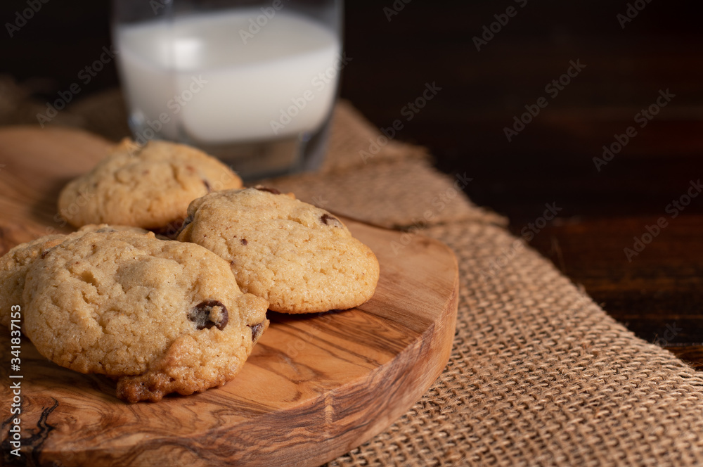 Homemade Chocolate Chip Cookies in a Group on a Rustic Wooden Cutting Board with a Glass of Milk