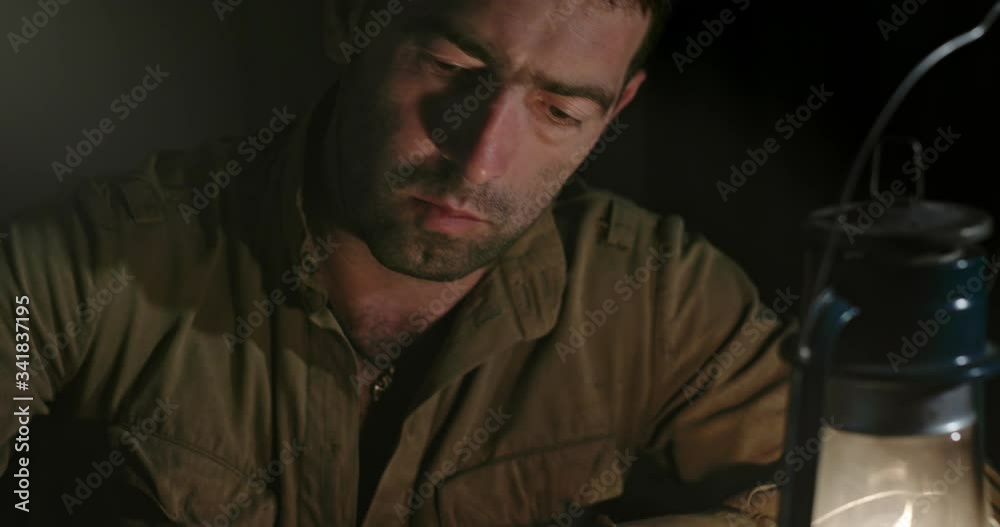 Soldier writing letter to home. Tilt down view of Soviet soldier sitting at table and writing message to home in dim light of oil lantern while taking break during World War II.