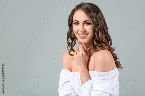 Beautiful young woman with curly hair on grey background
