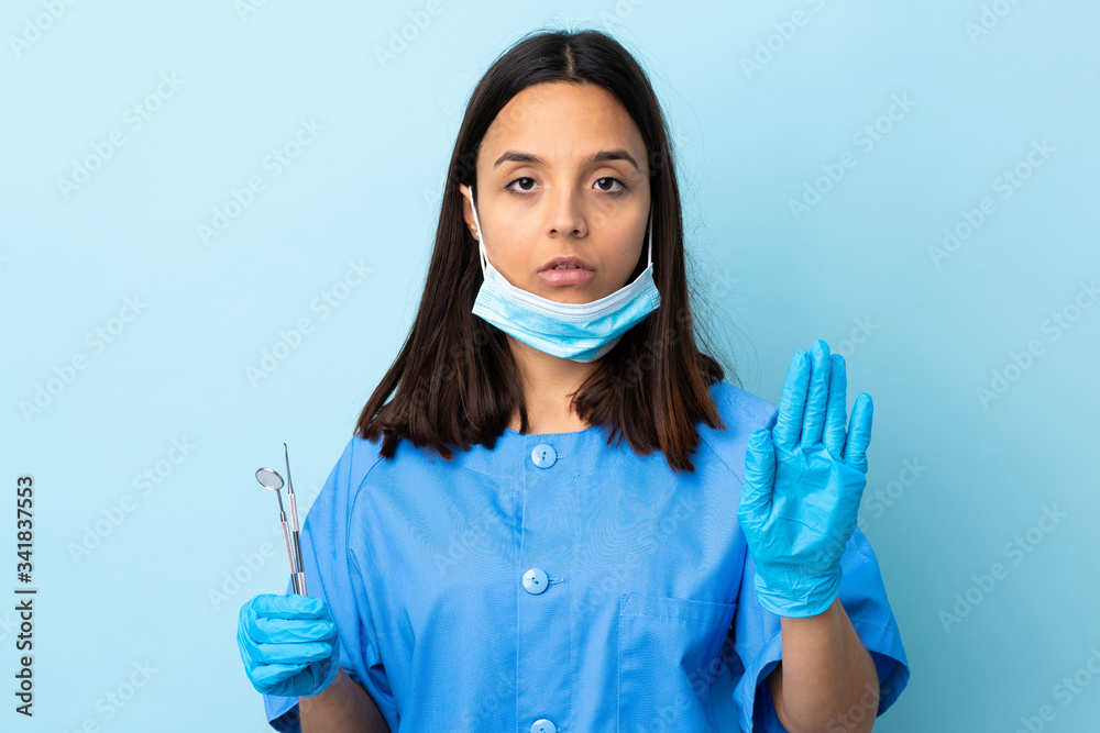 Young brunette mixed race dentist woman holding tools over isolated background making stop gesture Young brunette mixed race dentist woman holding tools over isolated background making stop gesture