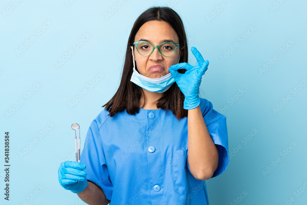 Young brunette mixed race dentist woman holding tools over isolated background showing a sign of silence gesture Young brunette mixed race dentist woman holding tools over isolated background showing a sign of silence gesture