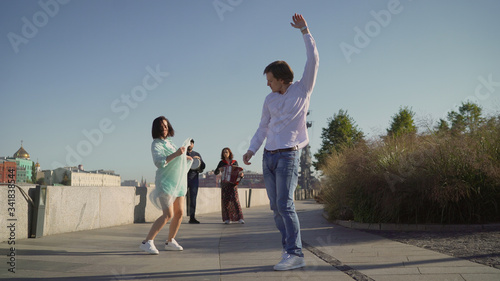 A young couple dancing to live music on the street. Musicians play, and a young couple dancing on the promenade. Music street performers couple with girl violinist and man guitarist on blue sky