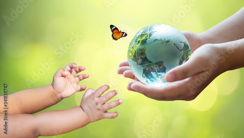 Fototapeta Naklejka Na Ścianę i Meble -  Adults are sending the world to babies. Concept day earth Save the world save environment The world is in the grass of the green bokeh background
