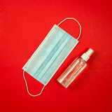 disinfectant antiseptic spray and protective medical respiratory mask on a red background, place for text, concept of prevention and protection against viral infections and healthcare