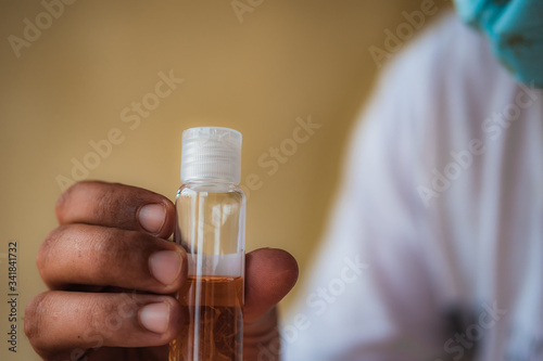 A person wearing face mask is showing a small tube filled with dark orange fluids. COVID-19 vaccine concept.