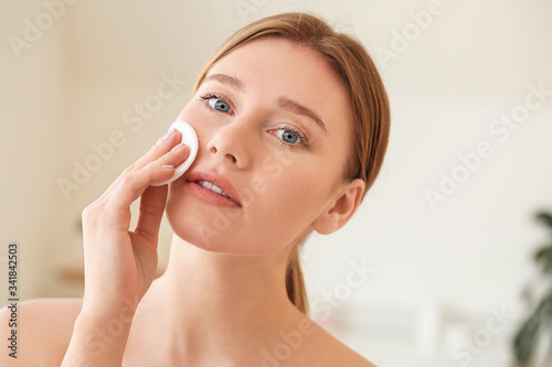 Beautiful young woman removing makeup at home