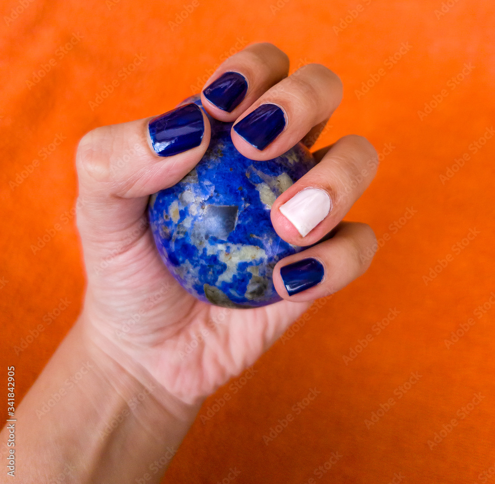 Fototapeta premium Hand with nail polish, blue and white, grabbing a sodalite rock.