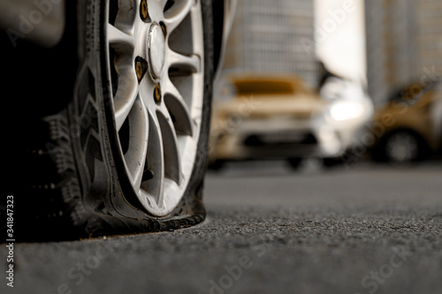 Car tire with a flat tire in the yard near a multi-storey building. Image of an accident, damage, breakdown for illustration on the topic of repair, insurance. Selective focus.