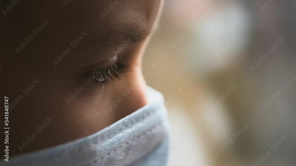 Little girl in a protective mask sits in quarantine at home. Stay at home, stay safe. Protection against virus and infection. Concept of coronavirus quarantine or covid-19.