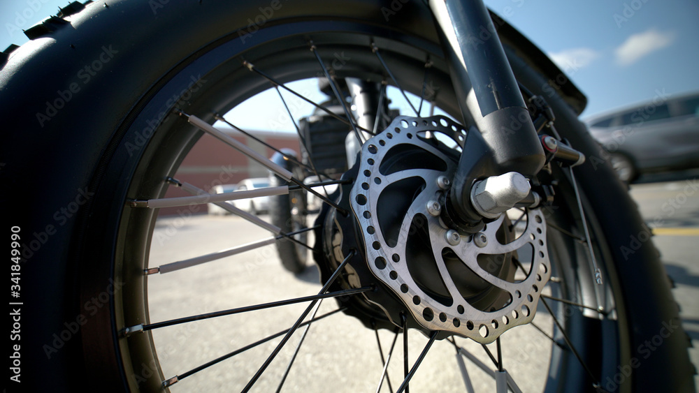 Fototapeta premium Focus on the tire of the electric bicycle with wheel motor at sunny summer day and light leaks and asphalt on the background. E bike motor with sun reflections on the parking near store. Close up.