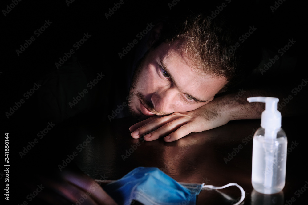 a doctor exhausted resting on the table at night quarantine lockdown for social distancing with the cellphone screen lighting , the chinstrap and the gel alcohol during the covid-19 pandemic a doctor exhausted resting on the table at night quarantine lockdown for social distancing with the cellphone screen lighting , the chinstrap and the gel alcohol during the covid-19 pandemic