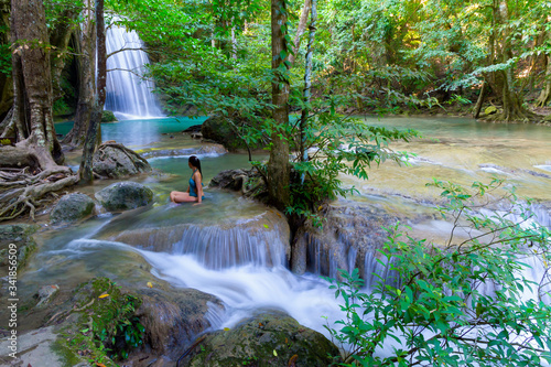 Traveler in blue swimsuit sit look Erawan Waterfall and natural
