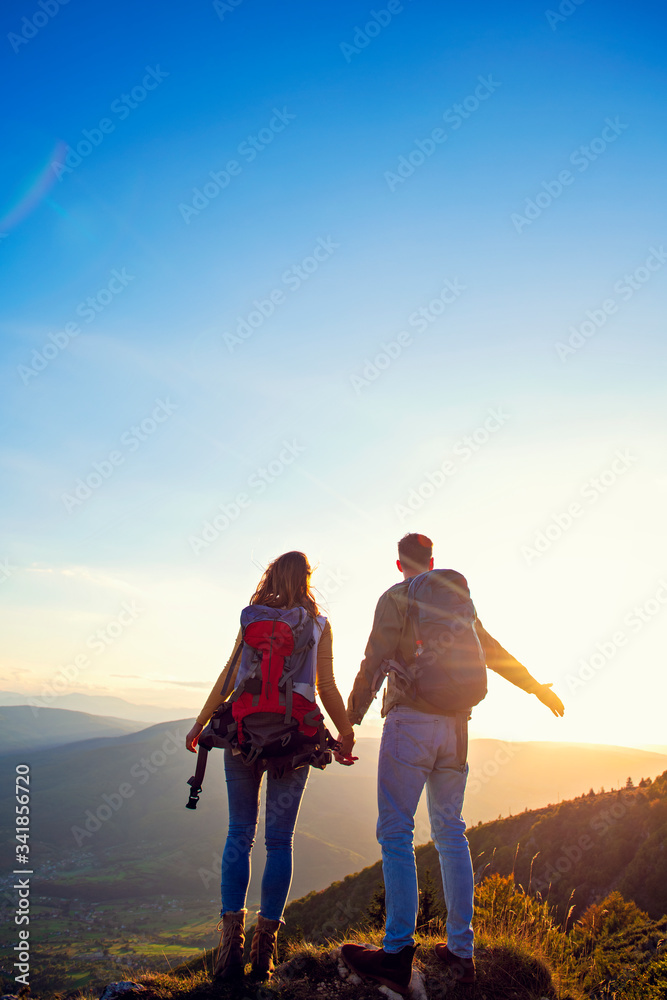 Fototapeta premium Hikers with backpacks relaxing on top of a mountain and enjoying the view of valley
